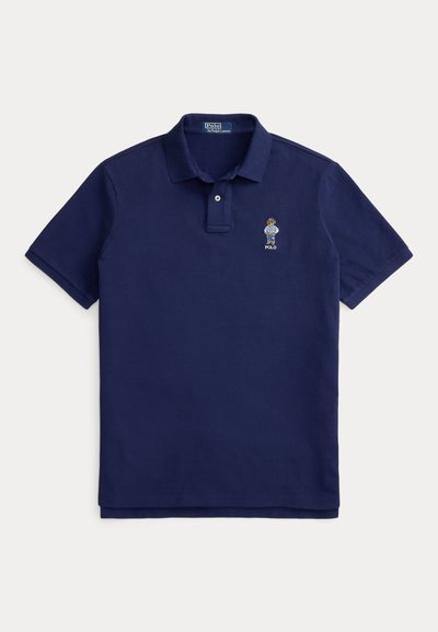 Μπλε σκούρο πόλο μπλουζάκι από βαμβάκι με κλείσιμο δύο κουμπιών. Διαθέτει κεντημένο έμβλημα στο αριστερό στήθος, κοντά μανίκια και ίσια γραμμή στο τελείωμα.