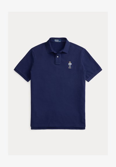 Μπλε σκούρο πόλο μπλουζάκι από βαμβάκι με κλείσιμο δύο κουμπιών. Διαθέτει κεντημένο έμβλημα στο αριστερό στήθος, κοντά μανίκια και ίσια γραμμή στο τελείωμα.
