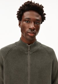 Olivgrüner Reißverschluss-Pullover mit hohem Kragen, gerippter Textur und kontrastierendem Reißverschluss. Einfaches, modernes Design mit eingesetzten Ärmeln.