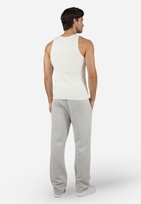 Top sin mangas blanco con textura acanalada, combinado con pantalones de chándal gris claro. El conjunto presenta un ajuste relajado y detalles de diseño mínimos.