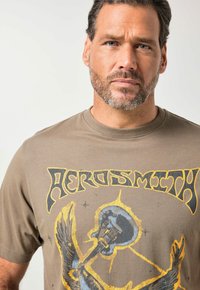 Camiseta de algodón marrón con un estampado gráfico en amarillo y negro que muestra un águila y una guitarra, con un diseño de cuello redondo.