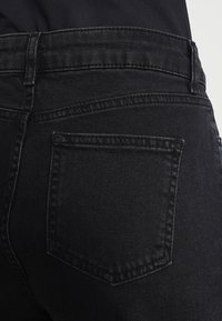 Schwarze Denim-Jeans mit einer Gesäßtasche und sichtbaren Nähten. Der Stoff hat eine glatte Textur und eine gleichmäßige Farbe ohne sichtbare Muster.