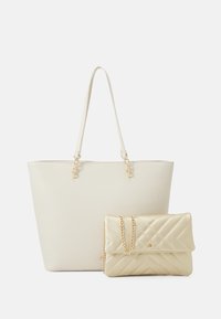 Beige läder tote-väska med guldfärgad hårdvara och dubbla remmar, i sällskap av en guldquiltad clutch med kedjesnodd.