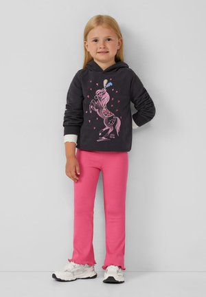 Schwarzer Hoodie mit buntem Einhorn-Graphic und Herzen; kombiniert mit leuchtend rosa gerippten Leggings mit Rüschenabschlüssen; weiße Sneaker.