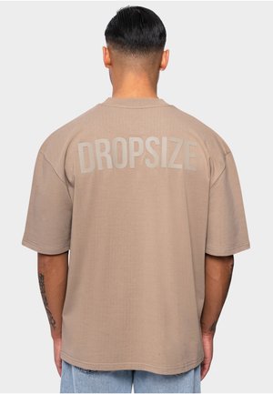 Brown oversized t-shirt with short sleeves, featuring the word "DROPSIZE" in large light gray letters on the back. Smooth texture.