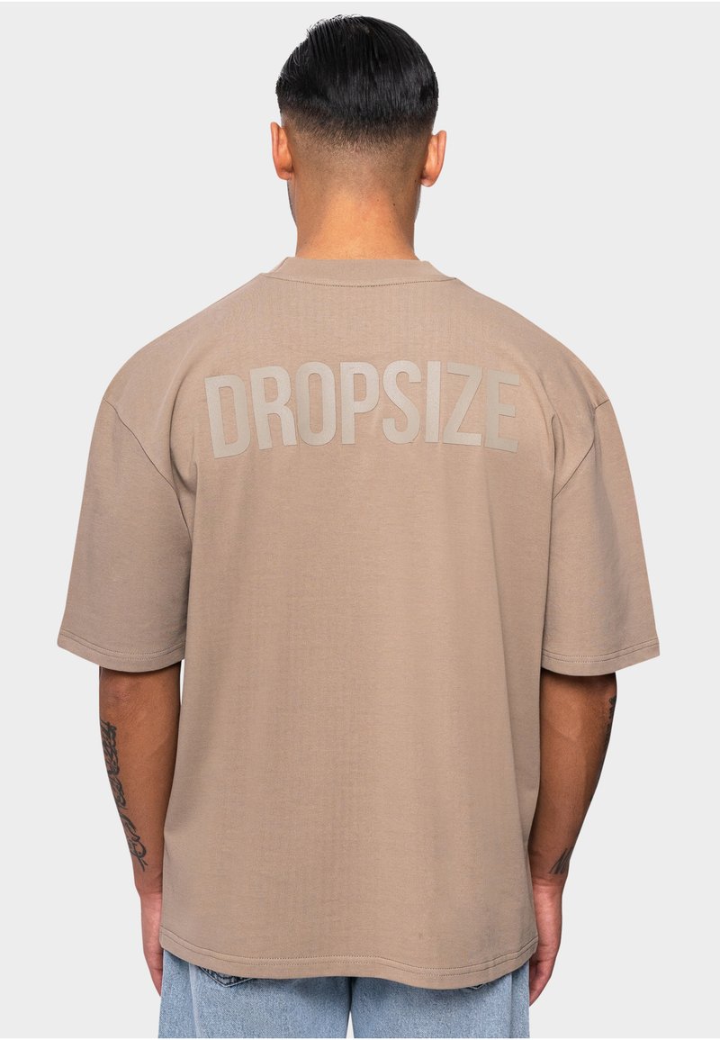 T-shirt oversize marron à manches courtes, arborant le mot "DROPSIZE" en grandes lettres gris clair au dos. Texture lisse.