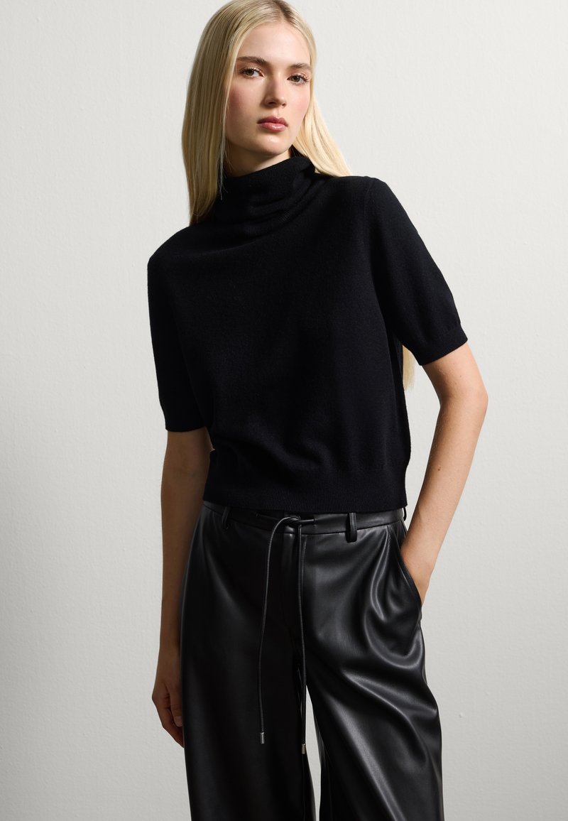 Maglione nero a maniche corte con collo alto realizzato in materiale morbido, abbinato a pantaloni in pelle neri a vita alta con una cintura regolabile.