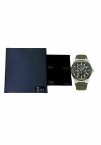 Reloj con correa de silicona verde, caja de acero inoxidable, esfera negra texturizada, acentos plateados y forma redonda. Incluye una caja de color azul oscuro.