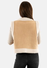 Chaleco de ante en tono arena con un suave cuello y forro de borreguillo color crema, que presenta un corte ajustado y una textura lisa.