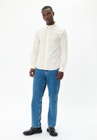 Helle beige Langarm-Hemden mit Kragen, kombiniert mit blauen Regular-Fit-Jeans und schwarzen Schuhen. Glatte Stofftextur.