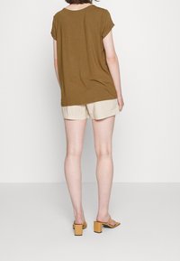 Hnědý krátký rukáv top s volným střihem, zkombinovaný se světlými béžovými šortkami. Modelka má na sobě hořčičkové sandály na blokovém podpatku.