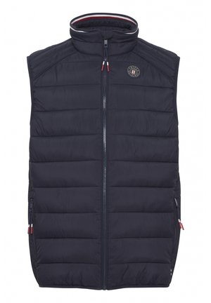 Námornícky modrá bezrukávová puffová vesta s vysokým golierom, vertikálnym prešívaním, bočnými zipsami a kruhovým logom na hrudníku.