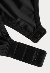 Soutien-gorge en tissu noir avec une texture lisse, bretelles ajustables et fermeture à crochets. Il présente un design simple sans motifs ni embellissements.