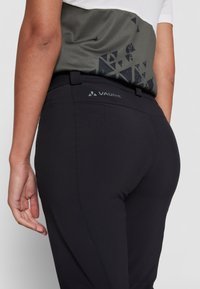 Black stretch pants with a smooth texture and a logo on the waistband. The design includes subtle stitching details and a fitted shape.