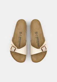 Paire de sandales Birkenstock beige avec une bride réglable à boucle unique et des semelles moulées, vues de dessus sur fond blanc.