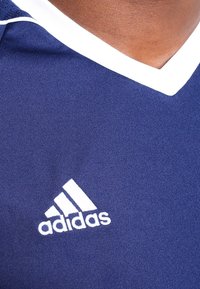 Navyblå idrottströja med vit V-ringning och vit Adidas-logotyp. Tillverkad av mjukt tyg, har korta ärmar och en figurnära design.