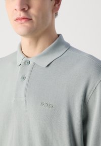 Világos zöld, textúrázott pólóing rövid ujjakkal, gallérral, két gombbal és hímzett "BOSS" logóval a bal mellen.