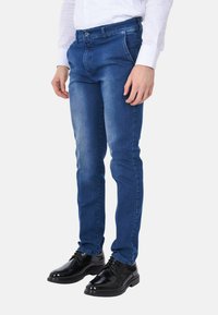 Jeans in denim blu con vestibilità slim, caratterizzati da un taglio dritto, design a cinque tasche e chiusura a bottone, abbinati a scarpe eleganti nere.