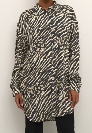 Chemise à manches longues noire et beige à imprimé animalier boutonnée, portée par une personne, avec col et poignets visibles.