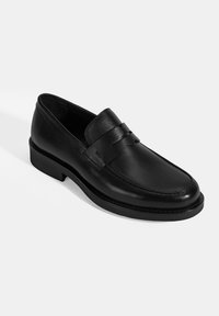 Schwarze Lederloafers mit glatter Oberfläche, versehen mit einem gesteppten Design, einer flachen Gummisohle und einem kleinen dekorativen Riemen oben.