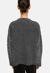 Szary dzianinowy sweter z luźnym krojem, prążkowaną fakturą i rozsypanymi cekinami na rękawach. Okrągły dekolt i nierówny detal u dołu.
