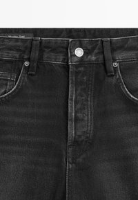 Jeans in denim nero con fronte piatto, chiusura con bottone in metallo, cinque tasche e cuciture a contrasto lungo le cuciture.