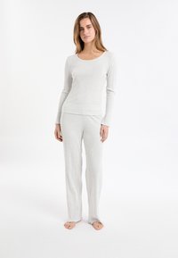 Kobieta stoi boso w jasnoszarej, prążkowanej bluzie z d�ługim rękawem oraz dopasowanych szerokich spodniach na białym tle.