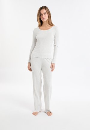 Kobieta stoi boso w jasnoszarej, prążkowanej bluzie z długim rękawem oraz dopasowanych szerokich spodniach na białym tle.