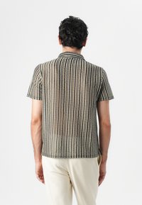 Kortermet skjorte med knapper i et gjennomsiktig stoff med vertikale striper i beige og svart. Har klassisk krage og subtil struktur.