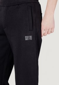 Pantaloni joggers neri con una texture morbida, dotati di una tasca laterale, vita elastica e un piccolo logo ricamato.