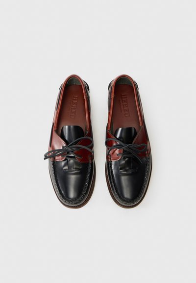 Zapatos de cuero con un diseño bicolor en negro y burdeos, con una textura suave, costuras en contraste y un detalle de cordones.