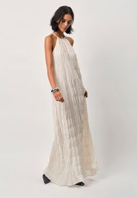 Helles, gefaltetes Maxikleid mit Halterneck-Design, das eine geschichtete Stoffstruktur aufweist. Kombination mit Schwarz-Weiß-Punkteschuhen.