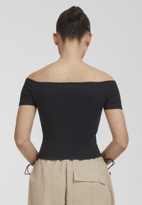 Black ribbed off-the-shoulder top with short sleeves, fitted design, and a smooth texture, paired with beige high-waisted pants.