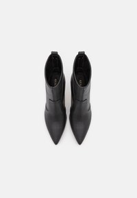 Bottines en cuir noir avec un bout pointu, une texture lisse, des découpes latérales et un talon court et arrondi. Présentent un logo doré à l'intérieur.