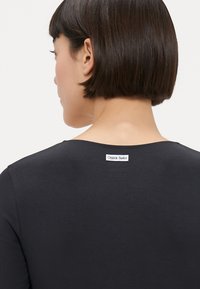 Chemise noire à col rond et manches courtes. Dispose d'une étiquette cousue à l'arrière près du col. Texture lisse.