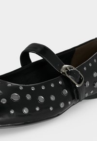 Μαύρη πλατφόρμα Mary Jane με ασημένιες κυκλικές τρουκς και ρυθμιζόμενο λουράκι πάνω από το πελματιαίο μέρος.