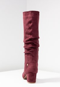 Botte montante bordeaux en suède doux, dotée d'un design froncé, d'un bout arrondi et d'un petit talon carré avec un accent doré.