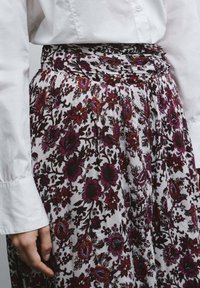 Bloemig patroon rok in het wit met paarse en zwarte accenten. Beschikt over een geplooide tailleband en een vloeiende stijl. De textuur lijkt lichtgewicht.