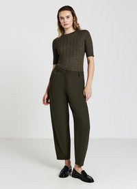 Haut en tricot à manches courtes vert olive avec un motif texturé, associé à un pantalon ample vert olive et des mocassins noirs.