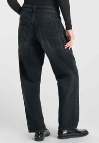 Des pantalons larges en denim noir dotés de deux poches arrière en angle, de coutures contrastées et d'une texture lisse. La taille se situe à la taille naturelle.