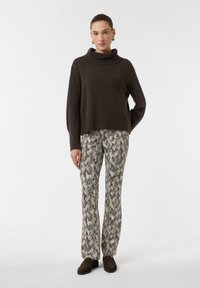 Brązowy dziany sweter z wysokim golfem w połączeniu z dopasowanymi, wzorzystymi spodniami w odcieniach kremu i szarości, z wzorem skóry węża.
