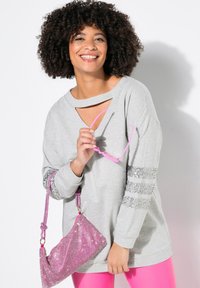 Felpa grigia chiaro con scollatura a taglio, strisce di paillettes argento sulle maniche, abbinata a una borsa luccicante rosa e occhiali da sole rosa.