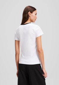 Hvit bomulls-t-skjorte med en tettsittende design, korte ermer og svart hals. Bakfra viser den en glatt, flat tekstur.