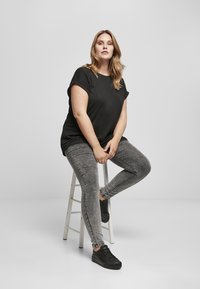 Fekete, rövidujjú felső, szürke, skinny farmerral és fekete sportcipővel párosítva. Az öltözet laza és testhez simuló, a modern megjelenést hangsúlyozza.