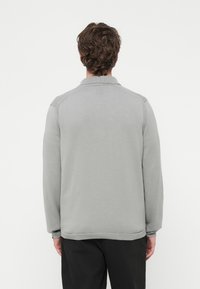 Szary pulower z długimi rękawami i kołnierzykiem. Posiada prążkowaną fakturę na mankietach i dole. Gładkie plecy z subtelnym wzorem w pobliżu kołnierza.