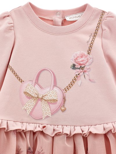 Robe rose à manches longues avec ourlet à volants, sac à main imprimé en forme de cœur avec nœud, chaîne en or et une rose rose avec ruban sur la poitrine.