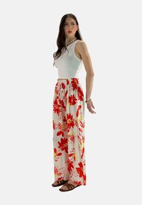 Floral maxi rok met rode en gele bloemen op een witte achtergrond, gecombineerd met een mouwloze witte top en bruine sandalen.