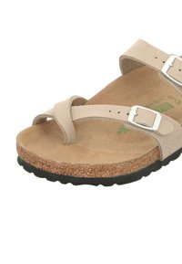 Beige suede sandal with cork footbed, two adjustable silver buckles, smooth texture, and a black rubber sole.