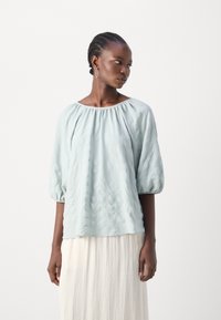 Lyseblå bluse med teksturfinish, båthals og balongermer. Kombinert med et flytende off-white skjørt.