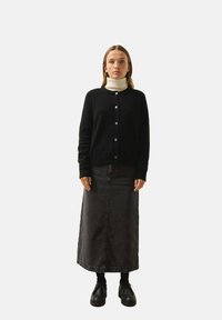 Svart stickad cardigan med kabelmönster, vit turtleneck, grå denimmaxikjol och svarta snörskor. Vita knappar på cardigan.
